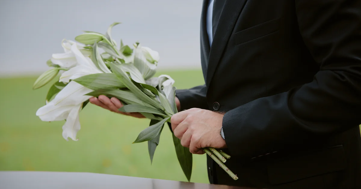 Ein Mann im dunklen Anzug hält Lilien in der Hand