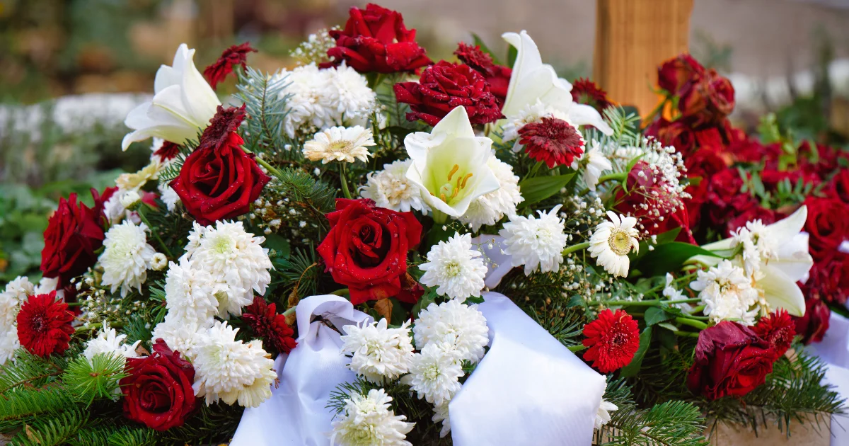 Blumengesteck aus weißen und roten Rosen mit weißem Band auf einem Sarg